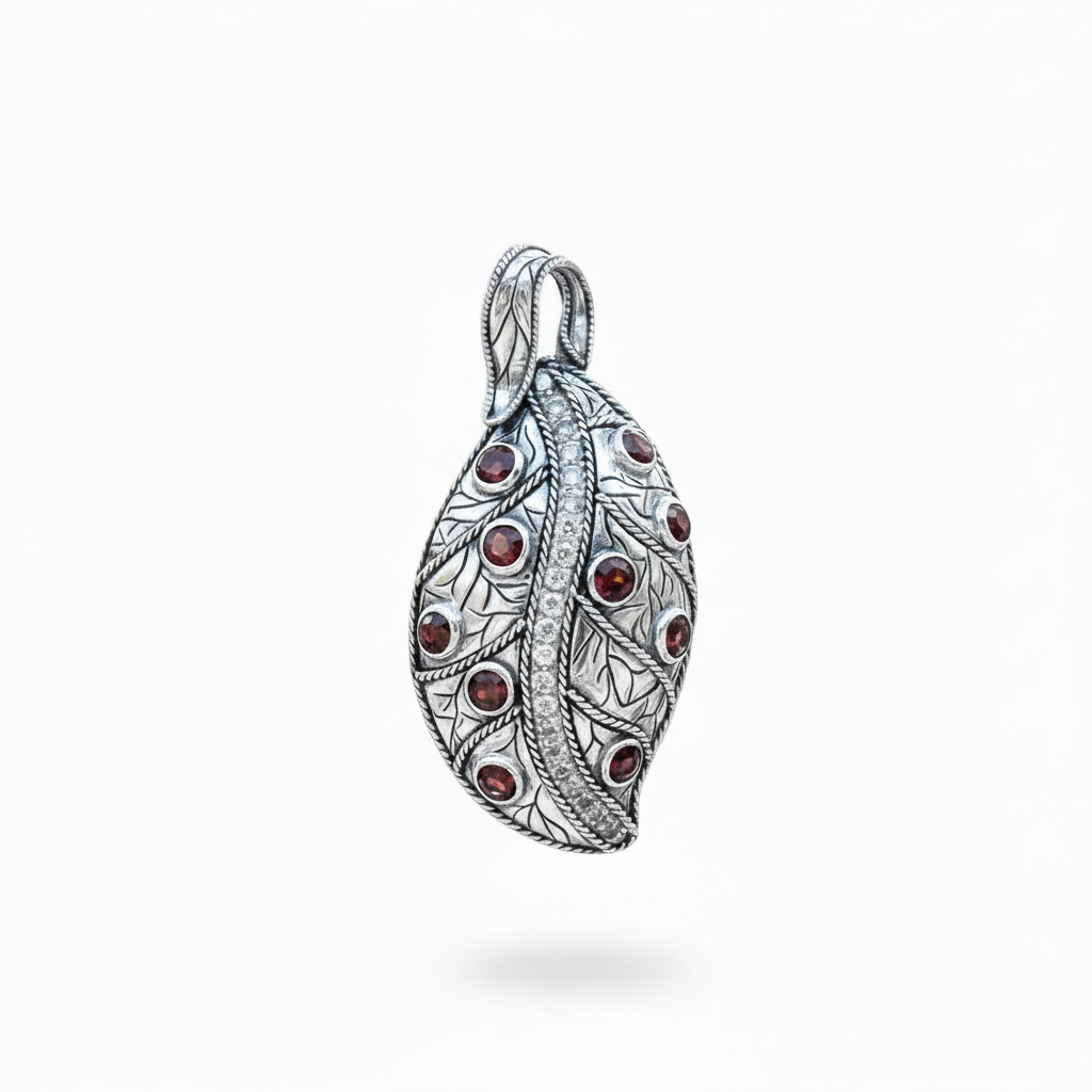 Ciondolo Daun Merah Balinesia, vista 3/4 su sfondo bianco con forma a foglia in argento 925 ossidato, granati rossi in castone e riga centrale di zirconi bianchi