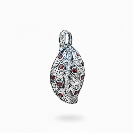 Ciondolo Daun Merah Balinesia, vista 3/4 su sfondo bianco con forma a foglia in argento 925 ossidato, granati rossi in castone e riga centrale di zirconi bianchi