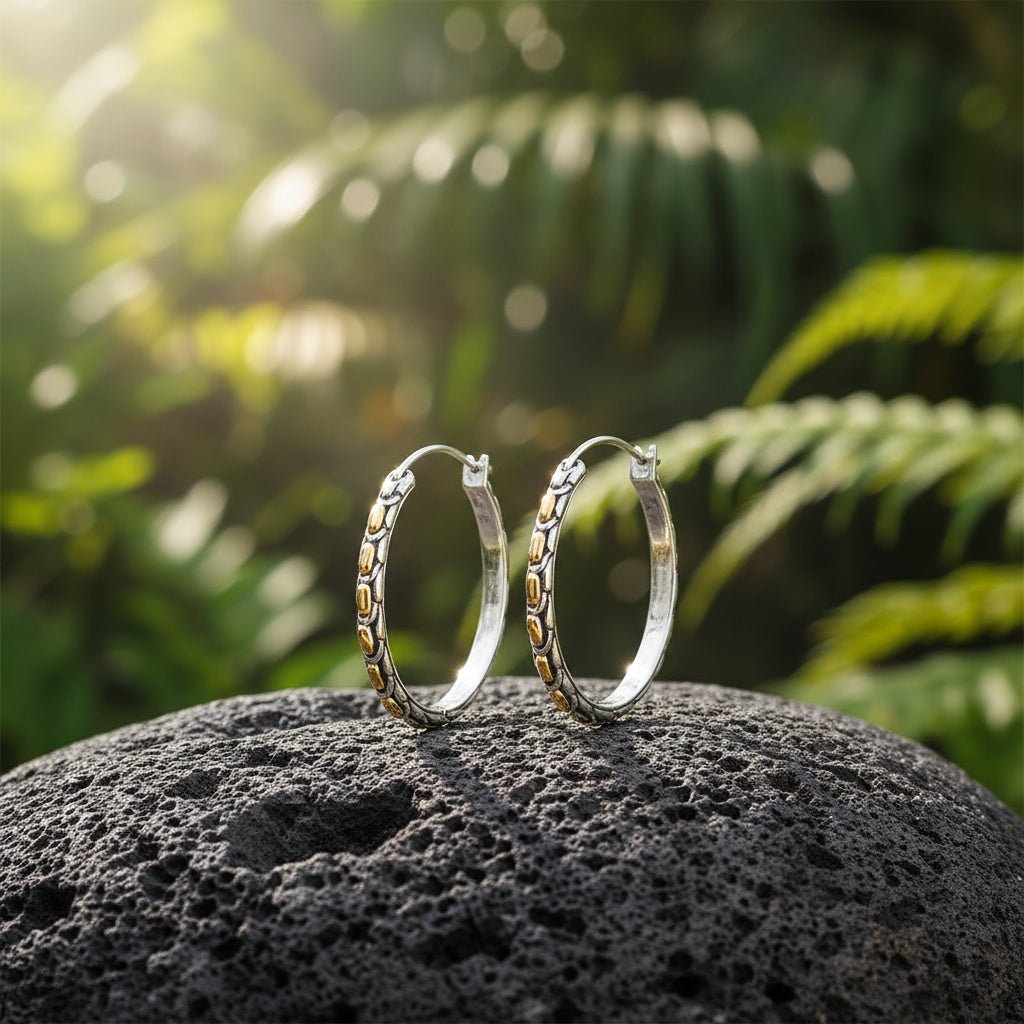 Coppia di Orecchini Golden Naga in argento 925 ossidato posata su pietra lavica balinese con foresta tropicale in sfondo, elementi ovali in oro 10K in luce naturale – Collezione Sisik Naga Balinesia