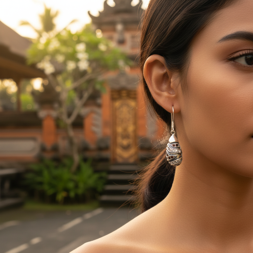 Orecchini Hujan Balinesia indossati su modella con sfondo tempio balinese al tramonto, goccia in argento 925 ossidato con zirconi rossi in primo piano