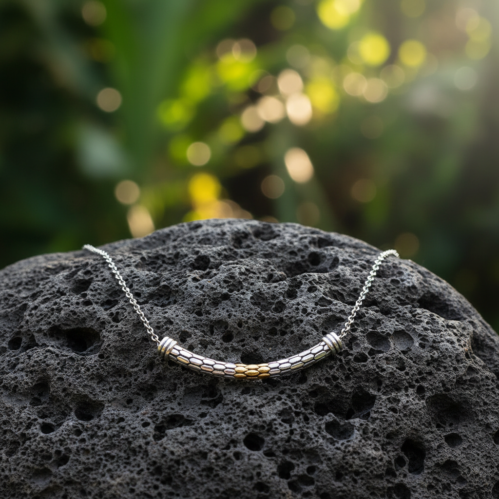 Collana Sisik Collezione Sisik Naga Balinesia, posata su pietra lavica con sfondo giungla bokeh, barra curva con texture a scaglie e accenti oro 18K in evidenza