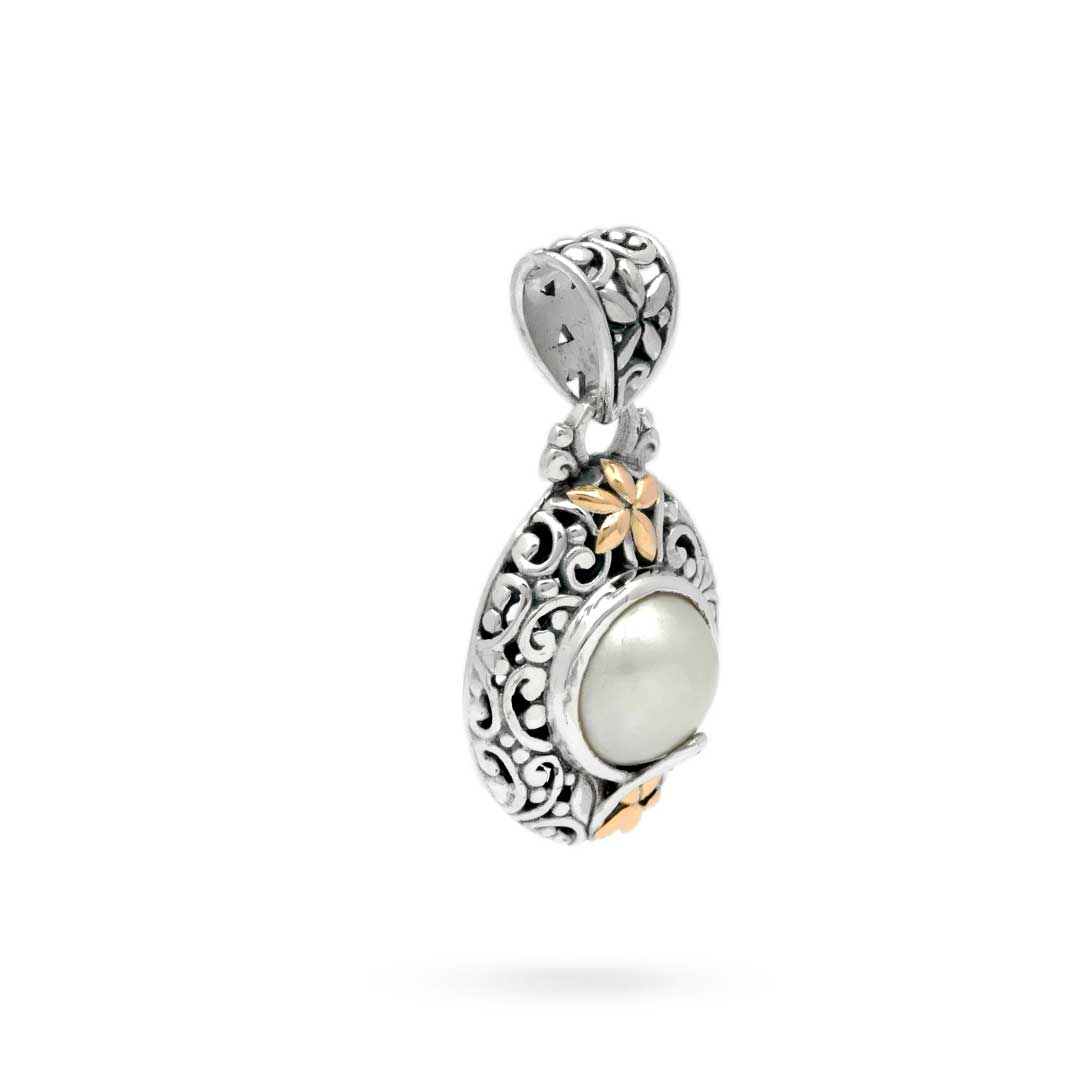 Ciondolo Lovina Balinesia, vista 3/4 opposta su sfondo bianco con fiorellino in oro 18k in alto, profilo convesso e motivi a volute in argento 925 ossidato