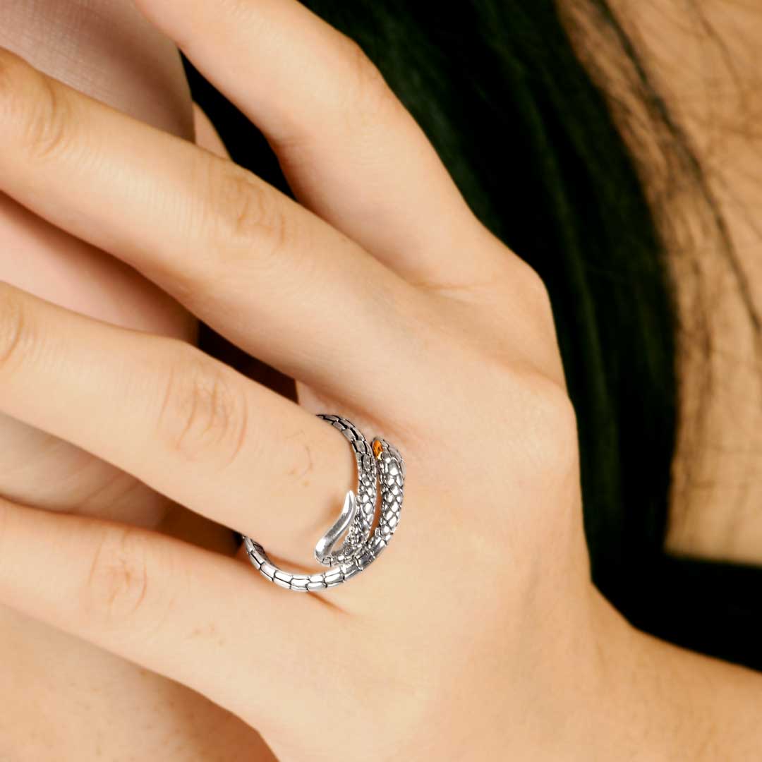 Anello Golden Ular Collezione Black Mamba Balinesia indossato su mano con sfondo foglia verde, doppio giro avvolgente con testa serpente, occhio in oro ambrato e lingua biforcuta in argento 925 ossidato