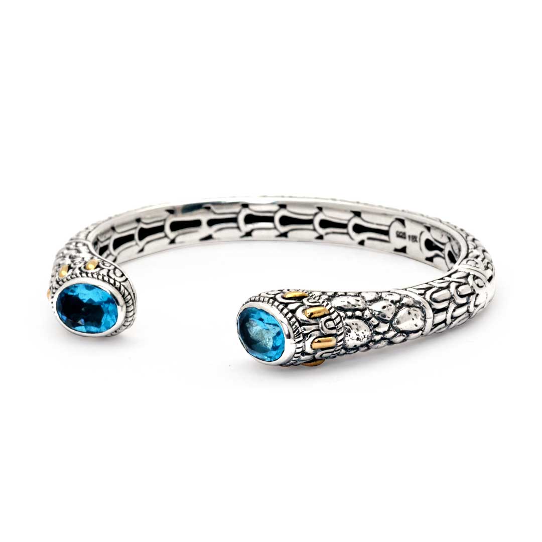 Bangle Naga Quarzo Blu Balinesia, vista tre quarti su sfondo bianco, dettaglio terminali con quarzi blu ovali e accenti oro su argento 925 ossidato