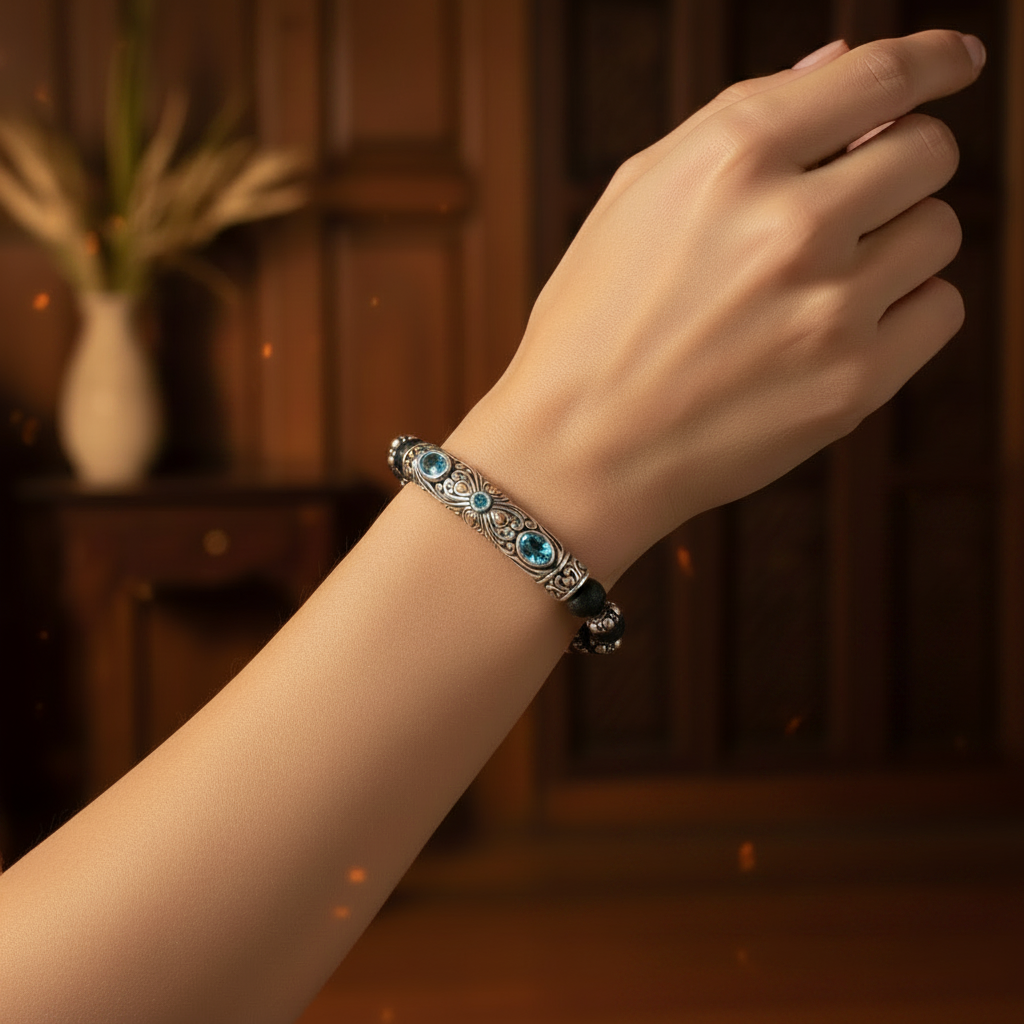 Bracciale Naga indossato al polso in ambiente caldo con candele — barra in argento con topazio blu London e filigrana balinese in luce soffusa, Balinesia