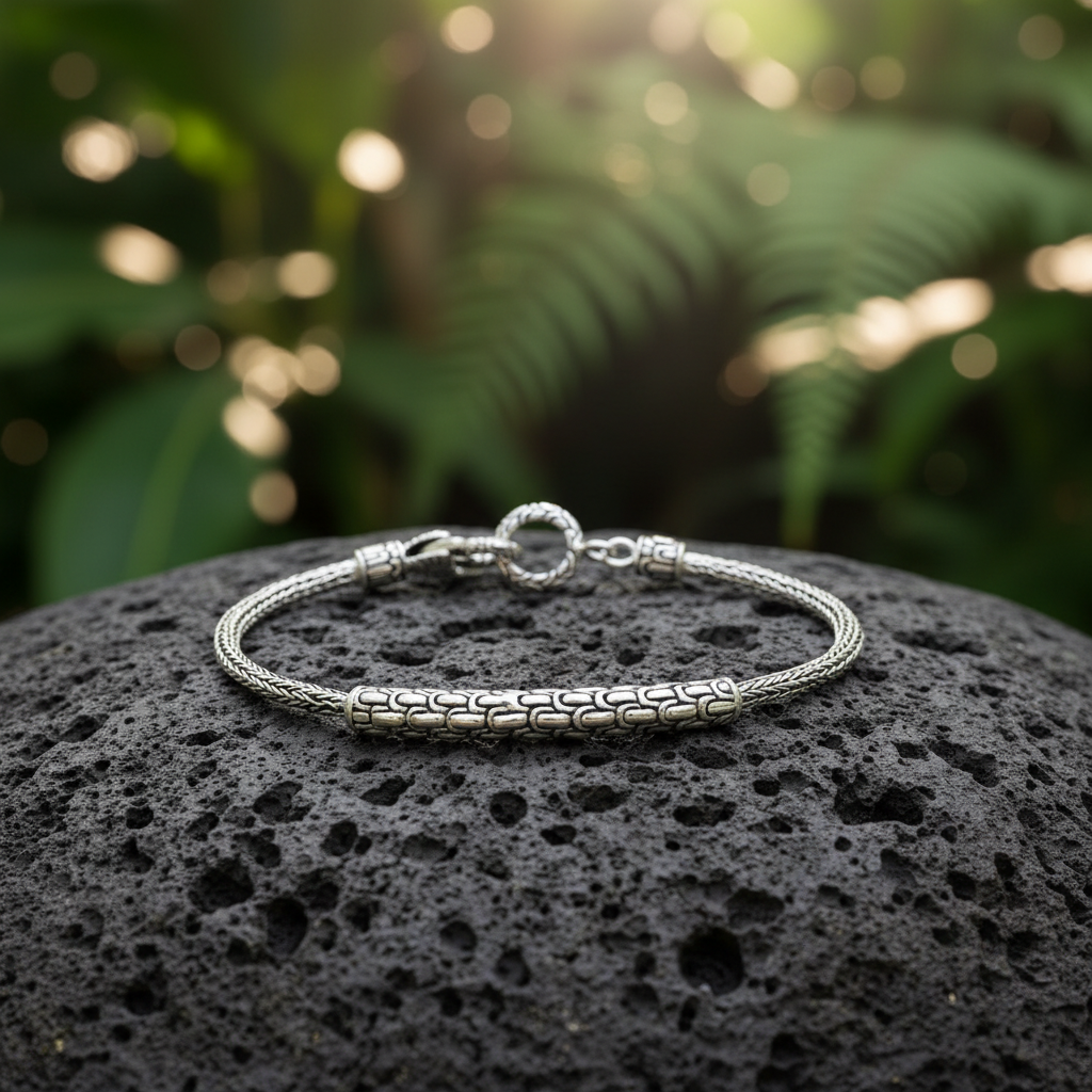 Bracciale Naga Tulang posato su roccia lavica nera con sfondo di giungla tropicale balinese — catena a spiga e barra Sisik Naga in luce naturale, Balinesia