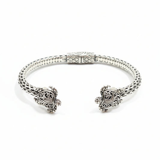 Bracciale Penyu Balinesia, vista frontale su sfondo bianco con bangle aperto in argento 925 ossidato, corpo a scaglie intrecciate e due tartarughe scolpite con filigrana a volute alle estremità