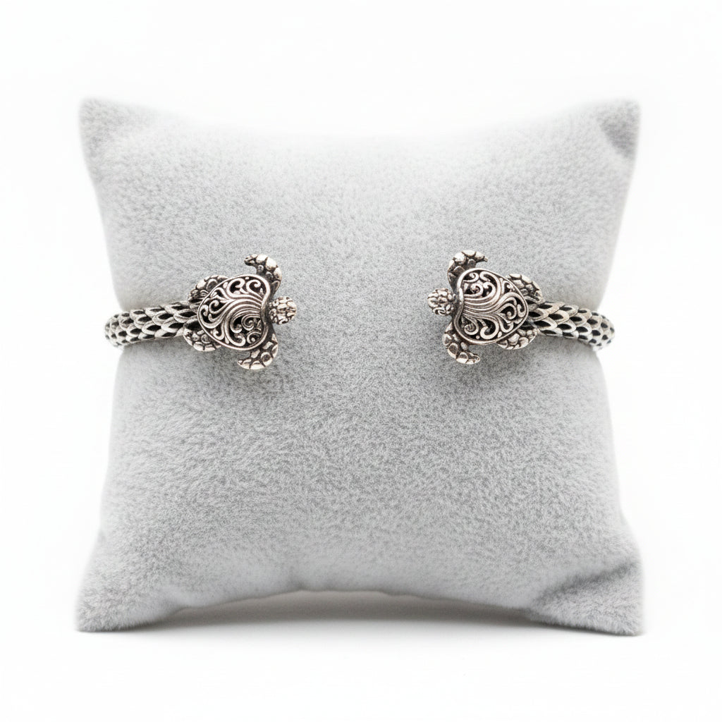 Bracciale Penyu Balinesia su cuscino espositore grigio, vista frontale con entrambe le tartarughe scolpite in argento 925 ossidato con filigrana balinese e corpo a scaglie intrecciate