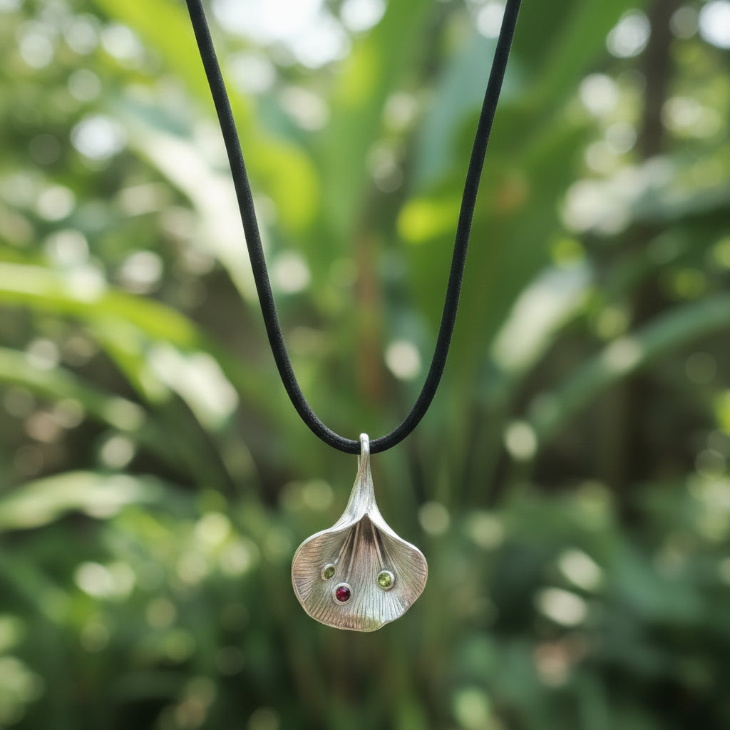 iondolo Fiore di Luce Balinesia con sfondo giardino tropicale balinese, petalo in argento 925 ossidato con due peridoti e granato arancio, cordino nero con chiusura in argento