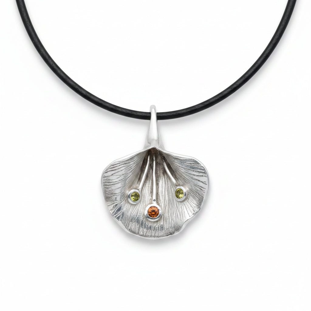 Ciondolo Fiore di Luce Balinesia su sfondo bianco con cordino nero, petalo in argento 925 ossidato con nervature incise a mano, due peridoti verdi e granato arancio incastonati, Collezione Essenza di Ubud
