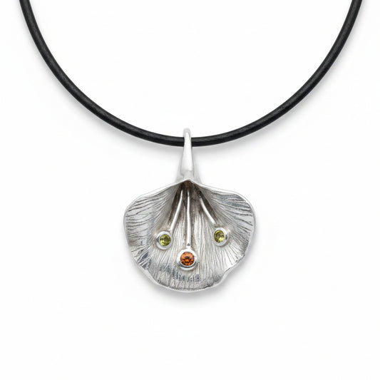 Ciondolo Fiore di Luce Balinesia su sfondo bianco con cordino nero, petalo in argento 925 ossidato con nervature incise a mano, due peridoti verdi e granato arancio incastonati, Collezione Essenza di Ubud