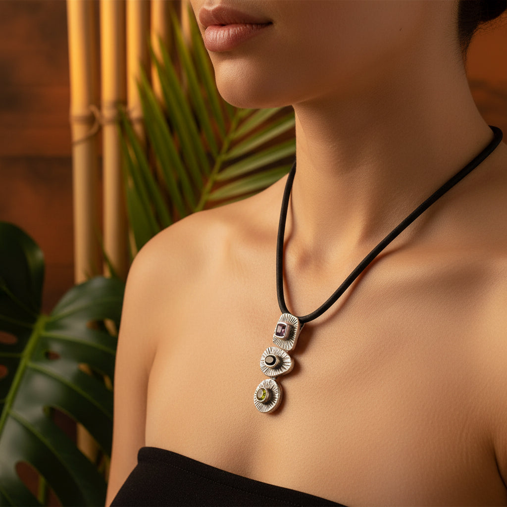 Ciondolo Tri Ratna Balinesia indossato da modella con sfondo bambù e foglia di palma, tre moduli in argento 925 con ametista, quarzo fumé e peridoto, Collezione Essenza di Ubud