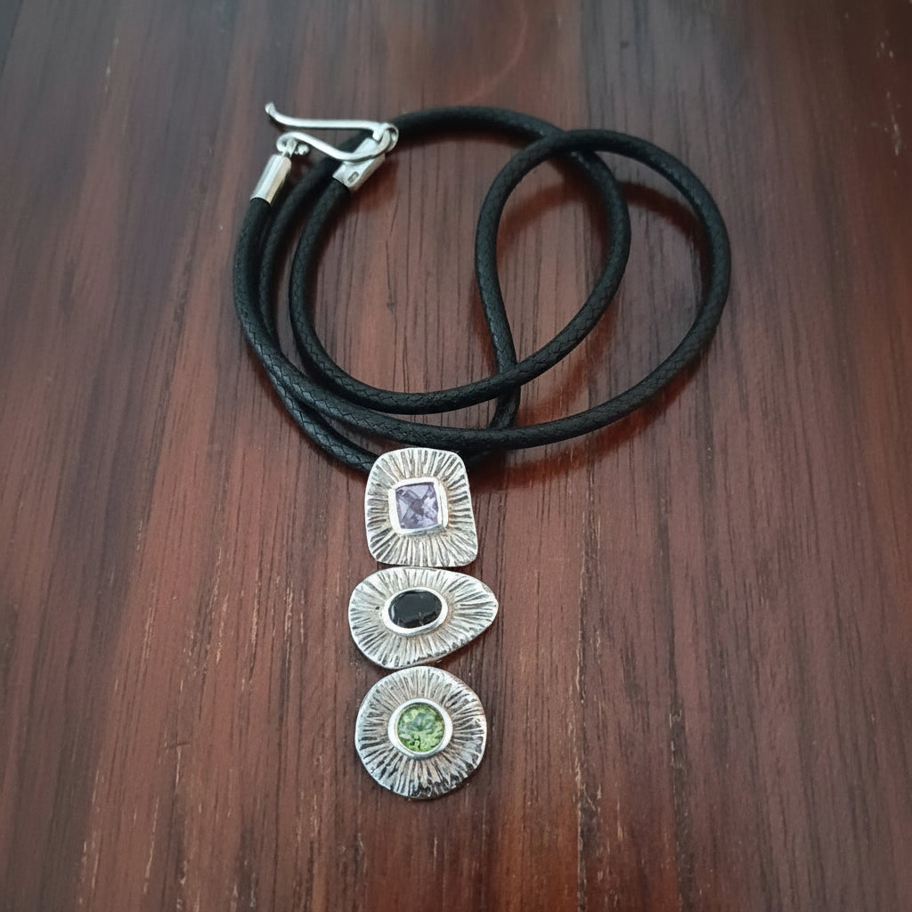 Ciondolo Tri Ratna Balinesia su legno scuro con cordino avvolto e chiusura a moschettone, tre moduli in argento 925 con texture a raggi solari e pietre naturali multicolore