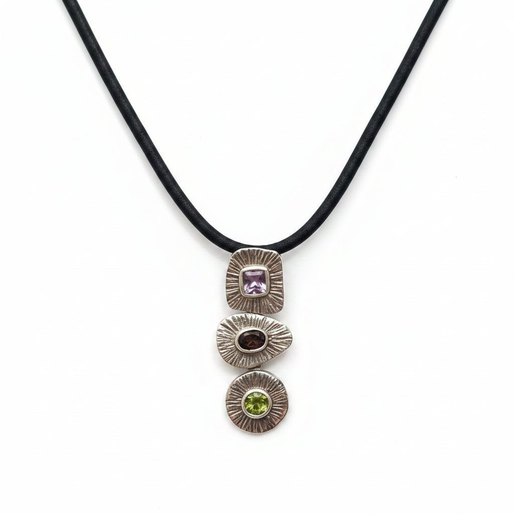 Ciondolo Tri Ratna Balinesia indossato da modella con sfondo bambù e foglia di palma, tre moduli in argento 925 con ametista, quarzo fumé e peridoto, Collezione Essenza di Ubud