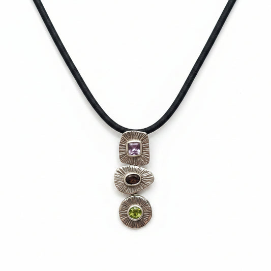 Ciondolo Tri Ratna Balinesia indossato da modella con sfondo bambù e foglia di palma, tre moduli in argento 925 con ametista, quarzo fumé e peridoto, Collezione Essenza di Ubud