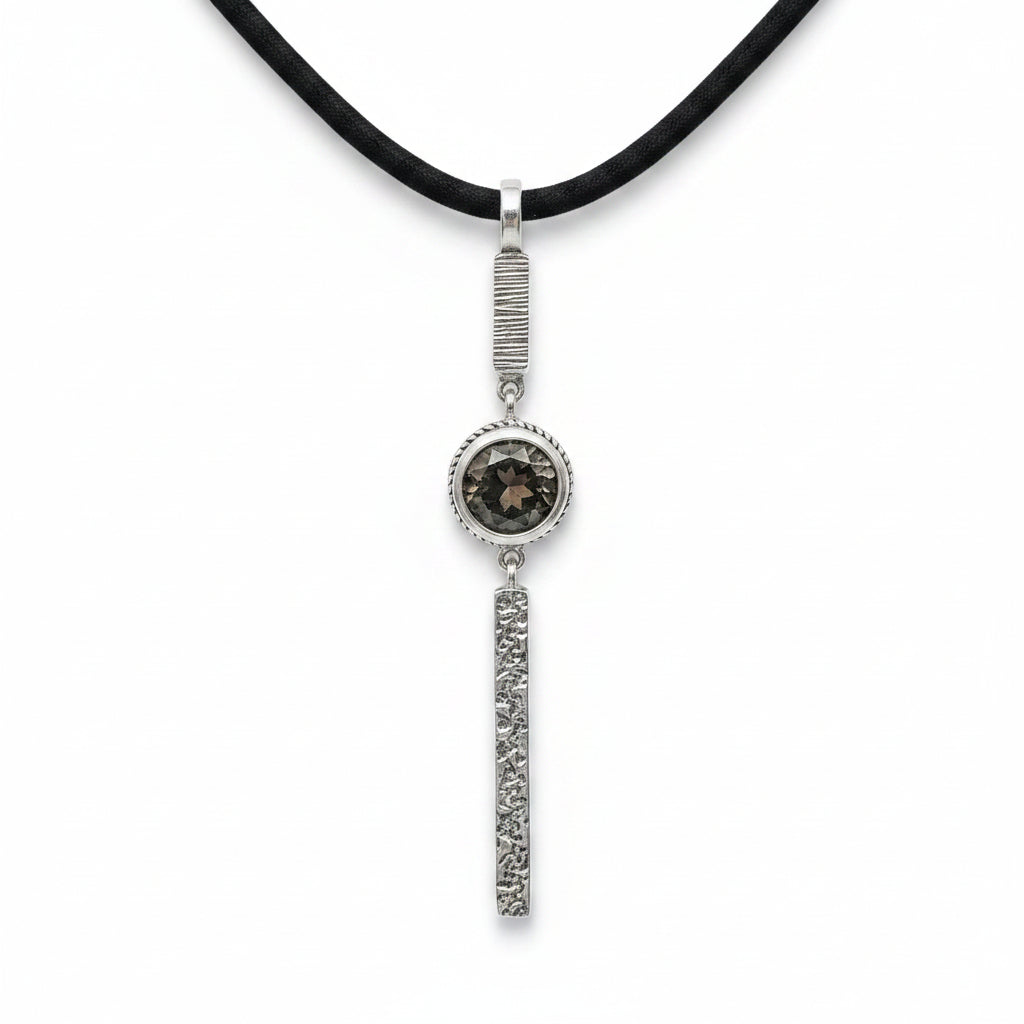 Collana Cawi Balinesia su sfondo bianco con ciondolo in argento 925 ossidato, barra superiore rigata, quarzo fumé rotondo in montatura a treccia e barra inferiore a texture vulcanica, cordino nero, Collezione Gunung Agung