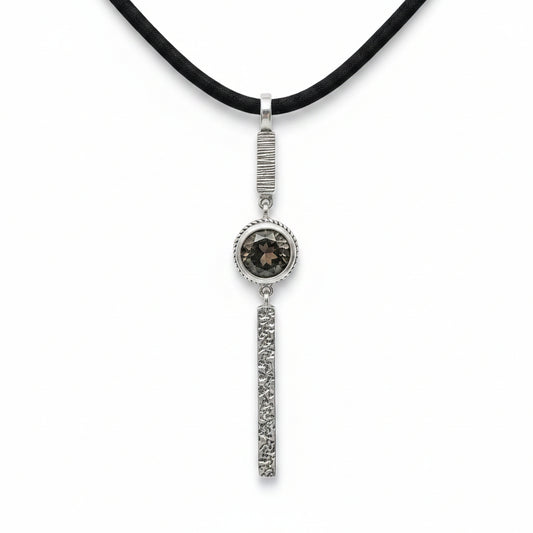 Collana Cawi Balinesia su sfondo bianco con ciondolo in argento 925 ossidato, barra superiore rigata, quarzo fumé rotondo in montatura a treccia e barra inferiore a texture vulcanica, cordino nero, Collezione Gunung Agung