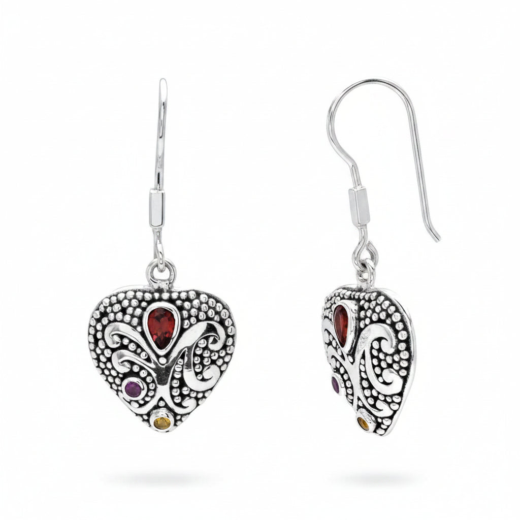Orecchini Cinta Tiga Warna Balinesia su sfondo bianco – coppia a cuore in argento 925 ossidato con granulazione e volute balinesi, granato rosso pear, ametista viola e citrino giallo – Collezione Viaggio a Celuk