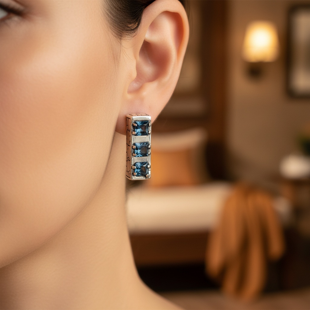 Orecchini Sinar Sky Blue Topaz indossati all'orecchio, barra argento 925 ossidato con texture Crocodile e 3 topazi blu quadrati a griffe – Balinesia